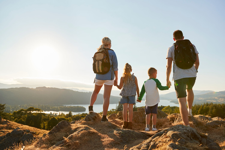 Rear View Of Family Standing At Top Of Hill On Hike Through Countryside In Lake District UK